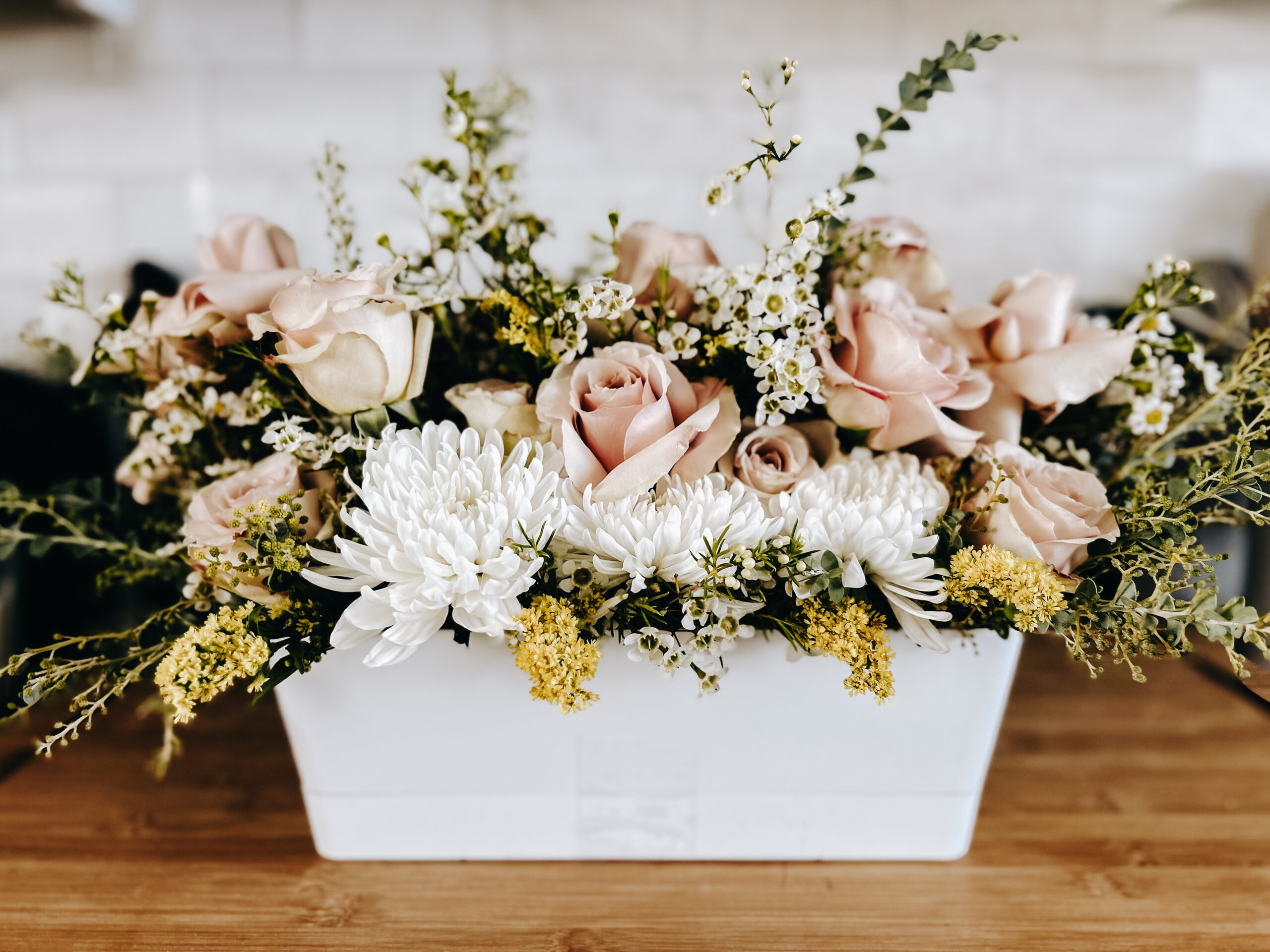 Blush garden roses, white chrysanthemums and wildflower greenery in a white ceramic planter