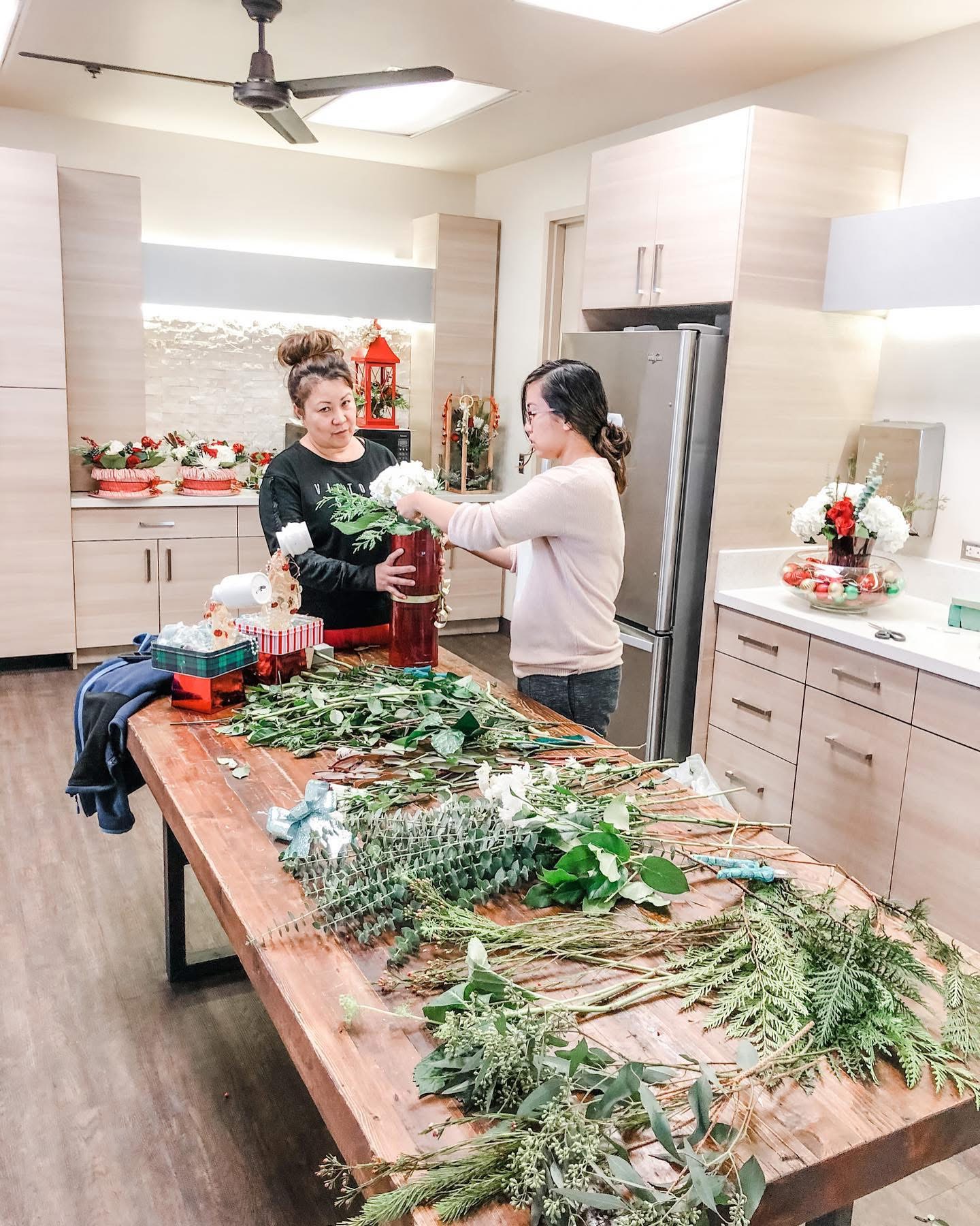 Two florists arranging white flowers in a red vase over a table of cleaned greenery stems in a San Diego floral studio