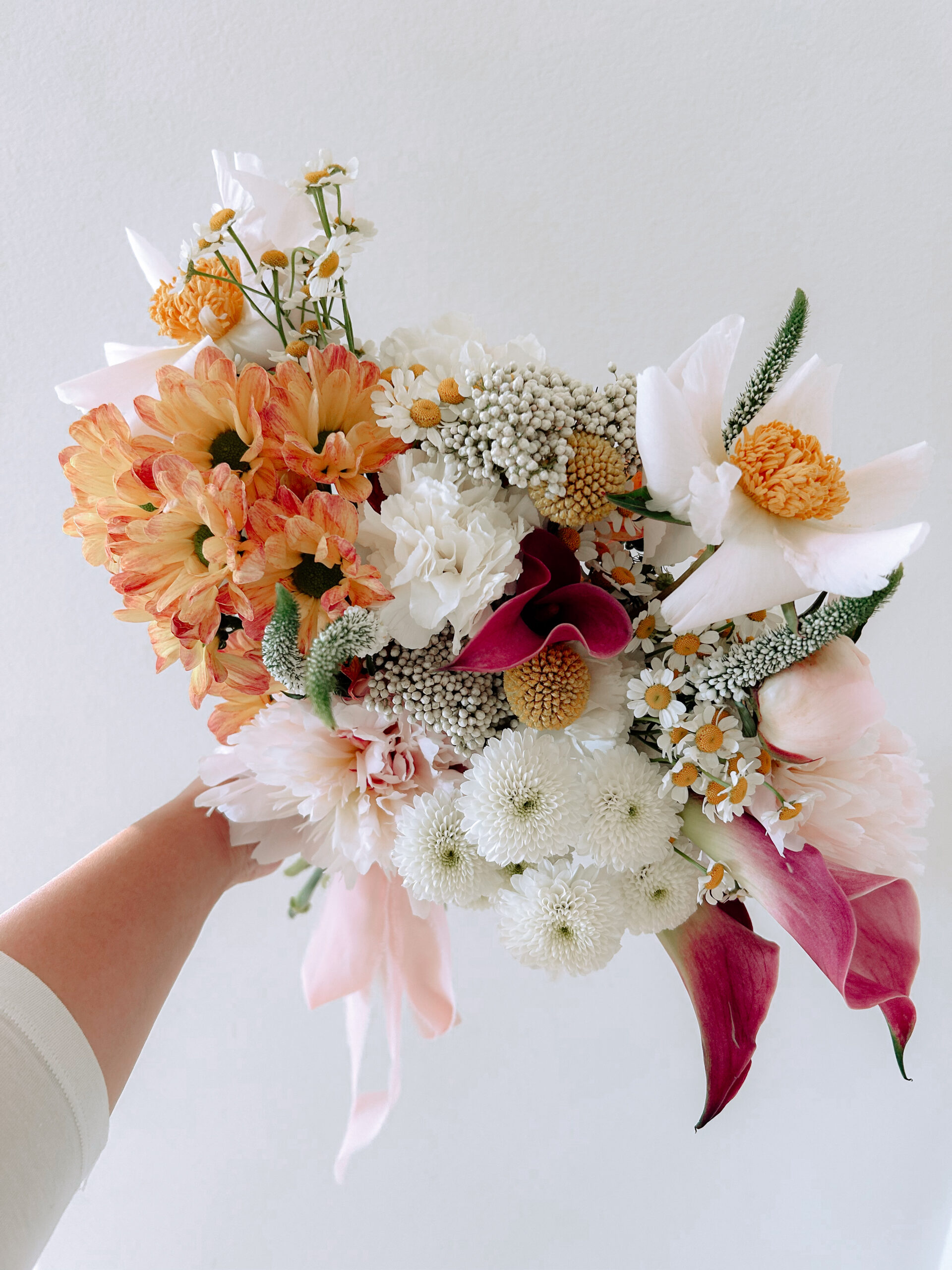 Colorful bridal bouquet of peach mums, white carnations, pink calla lilies and chamomile held up by a San Diego wedding florist