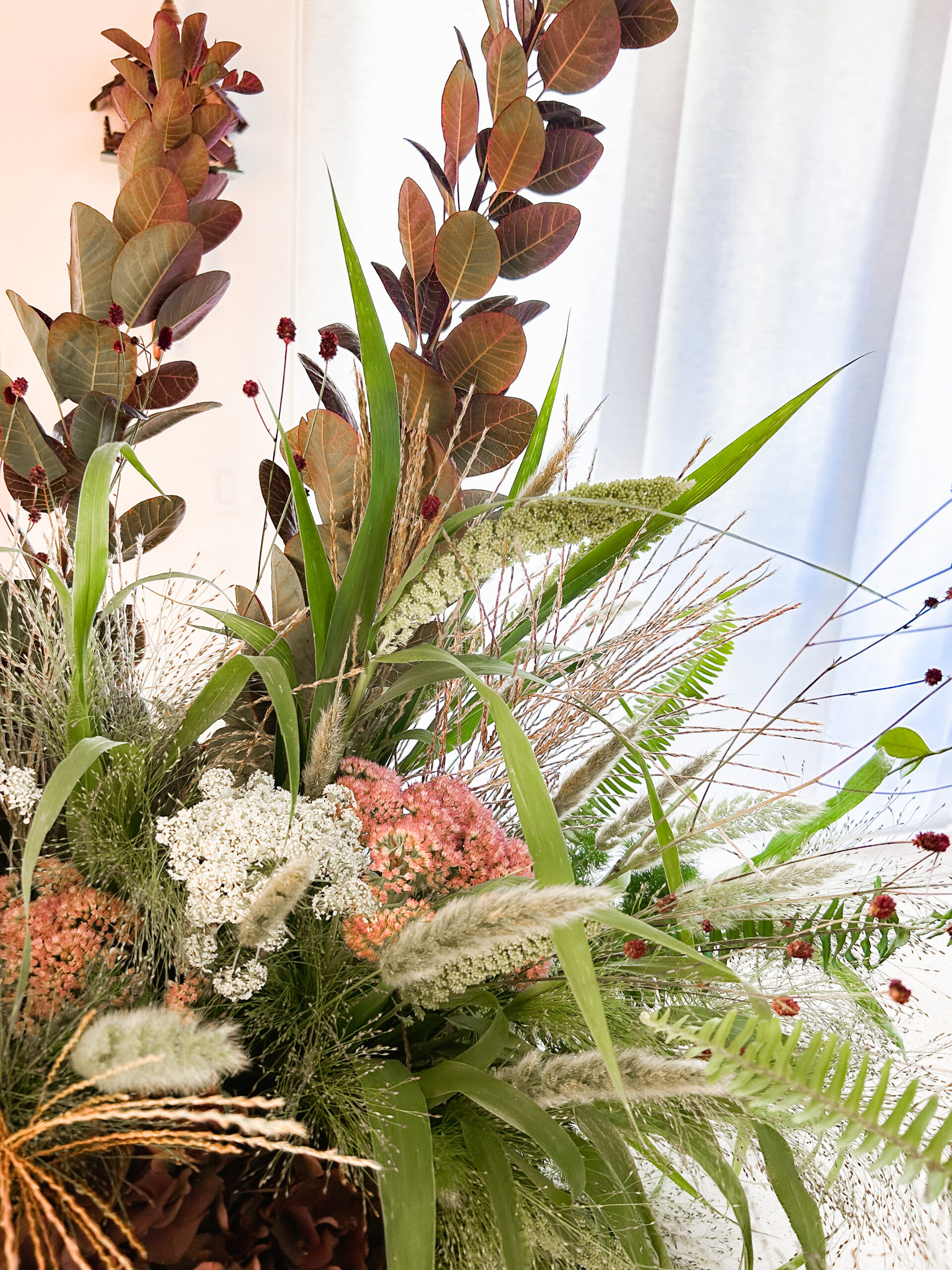 Burgundy smoke bush, ornamental grasses, and Queen Anne's lace in a textural fall wedding arrangement