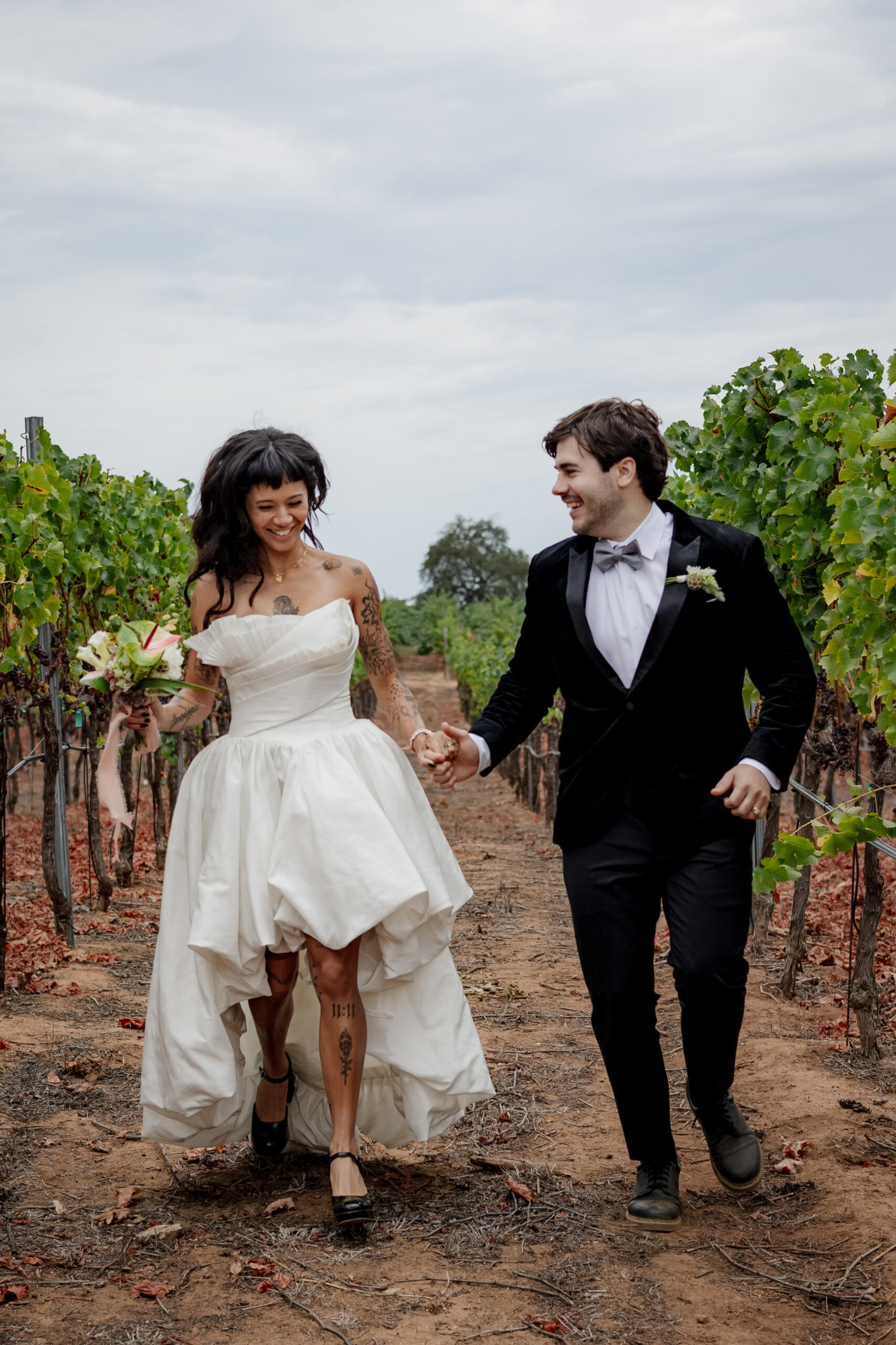 Couple walking through a vineyard with a fall wedding bouquet of anthurium and calla lily