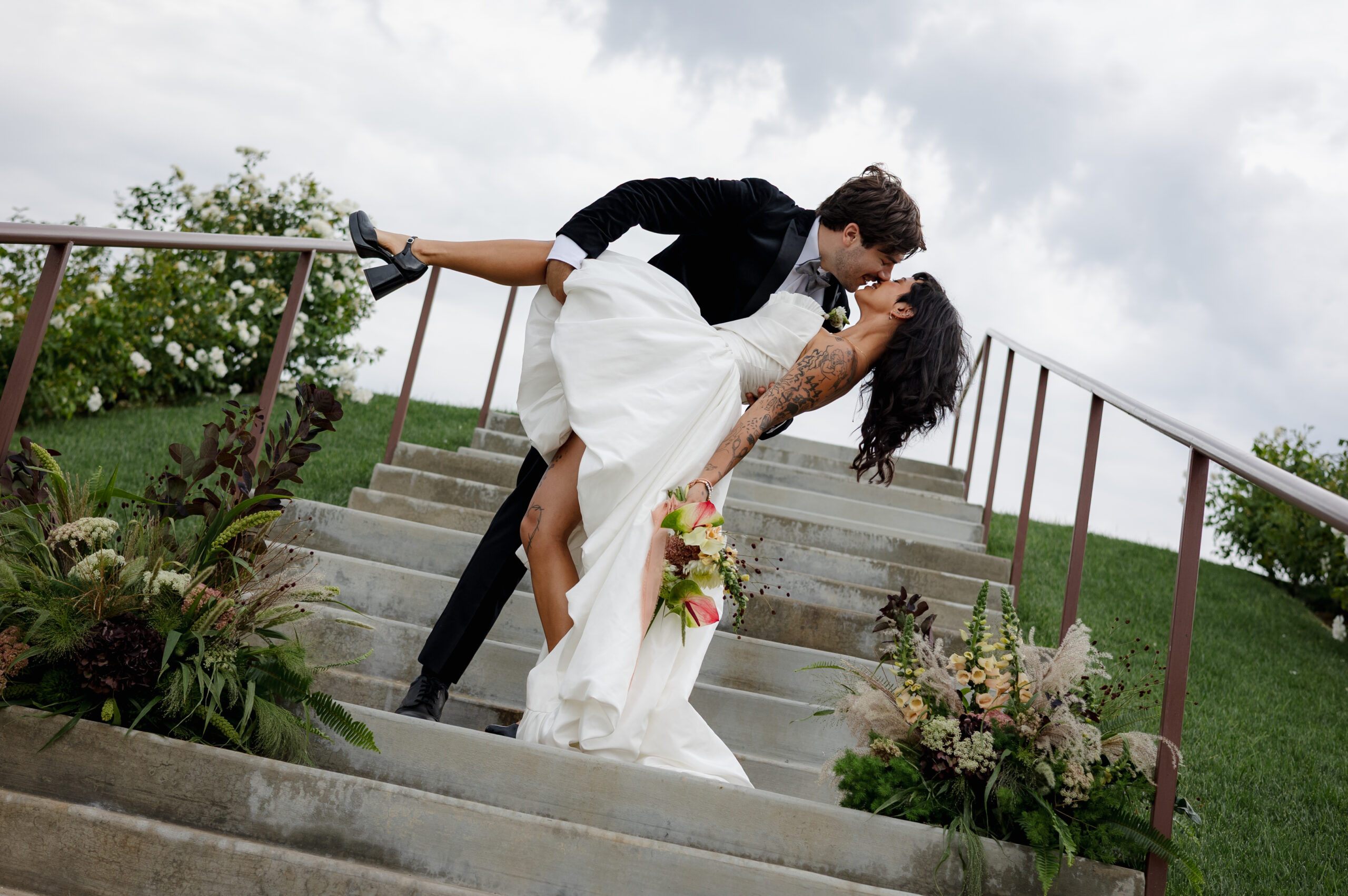 Dipped kiss on garden stairs framed by two lush arrangements of seasonal wedding flowers October favorites