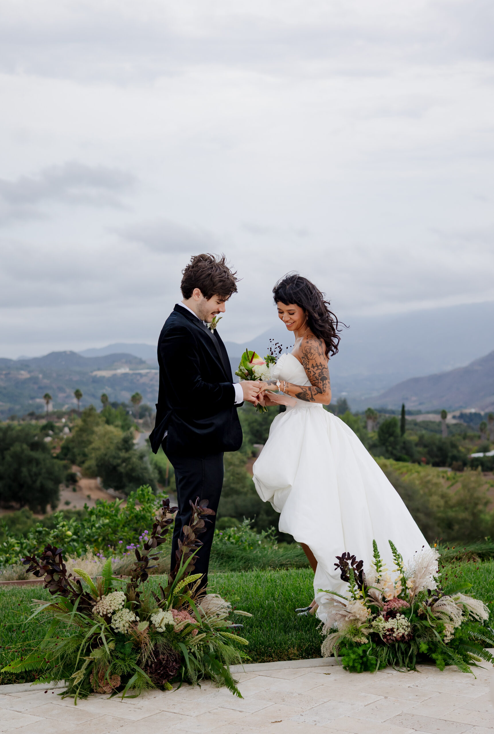 Groom placing a ring on his bride's hand beside seasonal wedding flowers October blooms