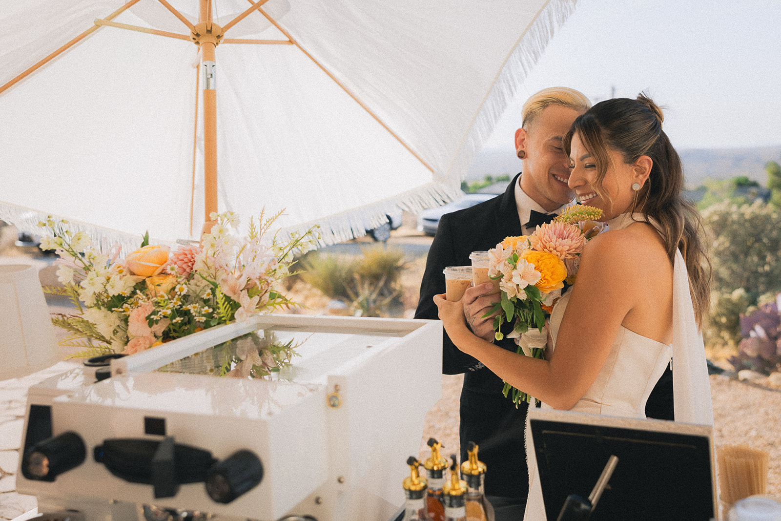 Groom kisses his bride's forehead as she holds her bouquet next to a coffee cart styled with fresh flowers