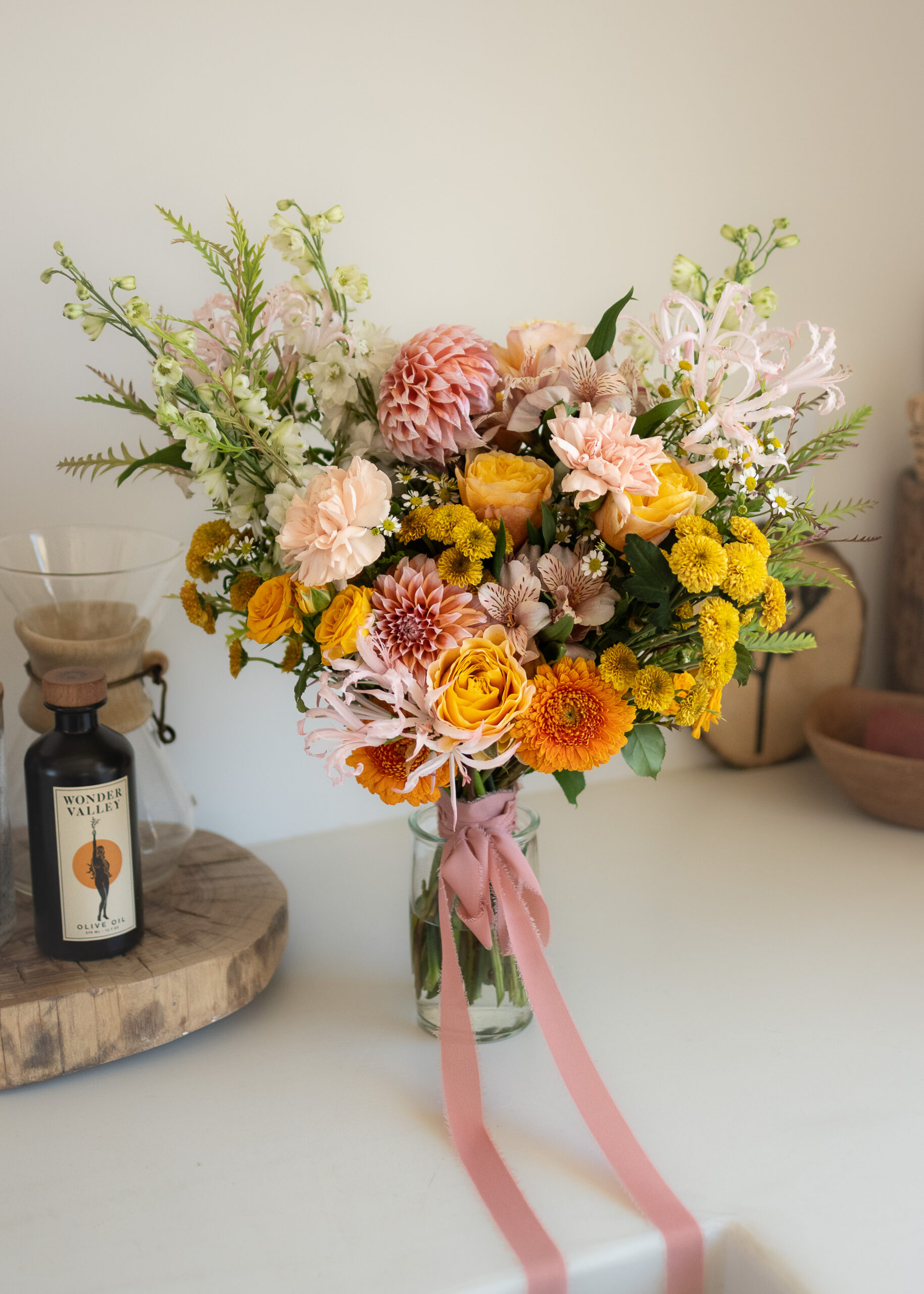 Garden-style bridal bouquet with pink ribbon in a glass vase on a counter, prepped as part of wedding florist services
