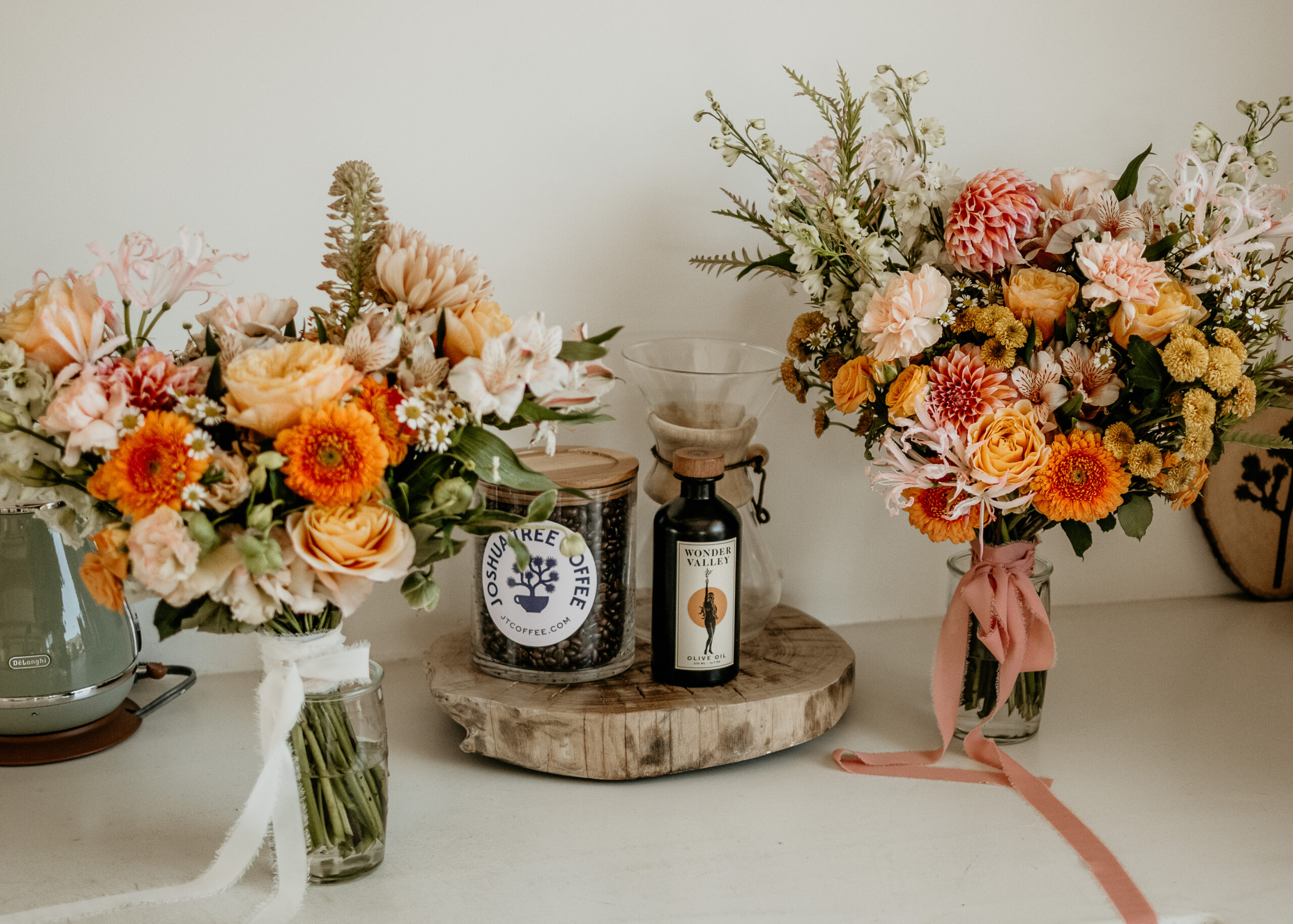Two garden bouquets in glass vases with ribbon beside coffee bottles, arranged by full-service wedding florist services