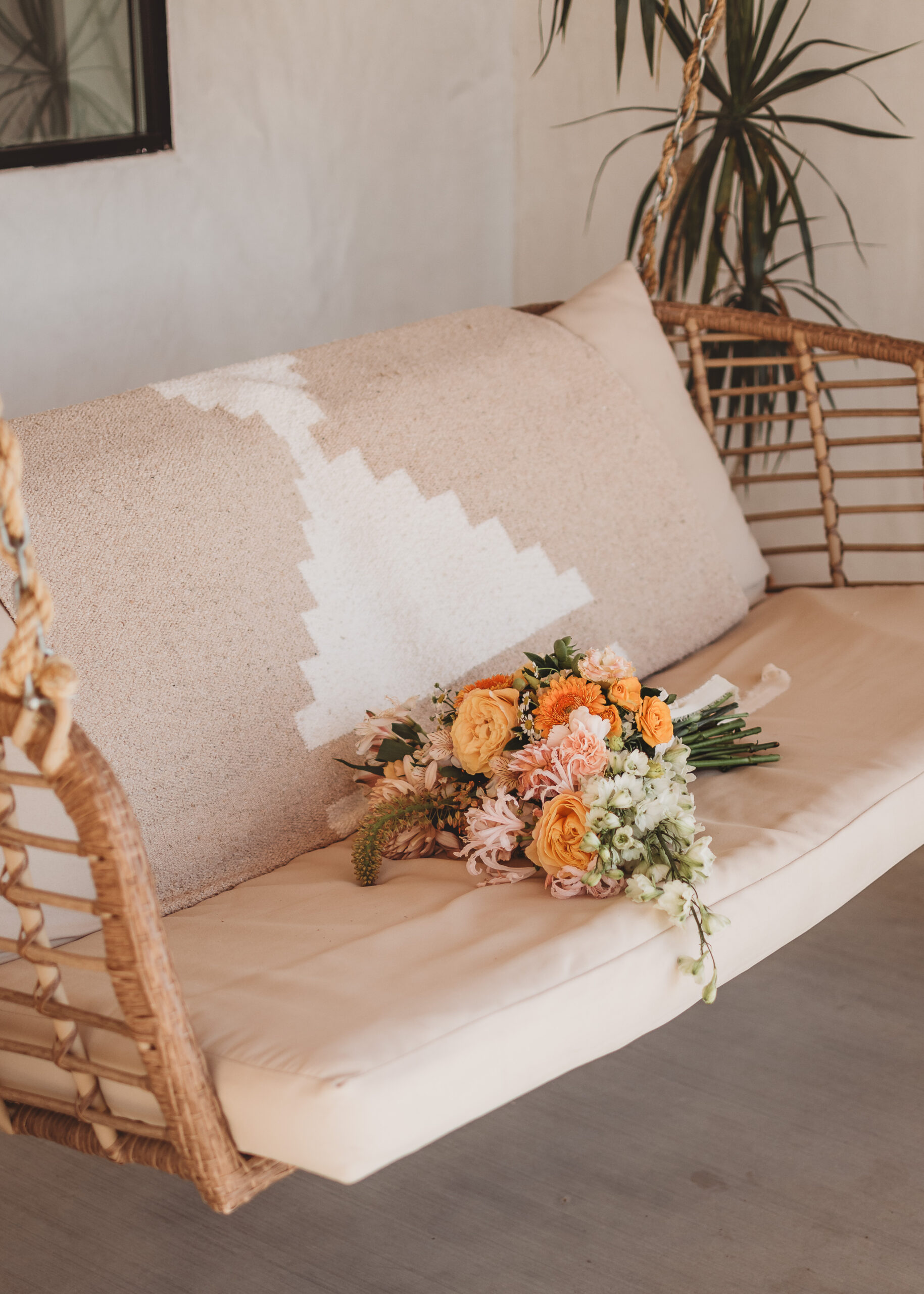 Peach and orange bouquet with trailing greenery resting on the cushion of a rattan hanging swing
