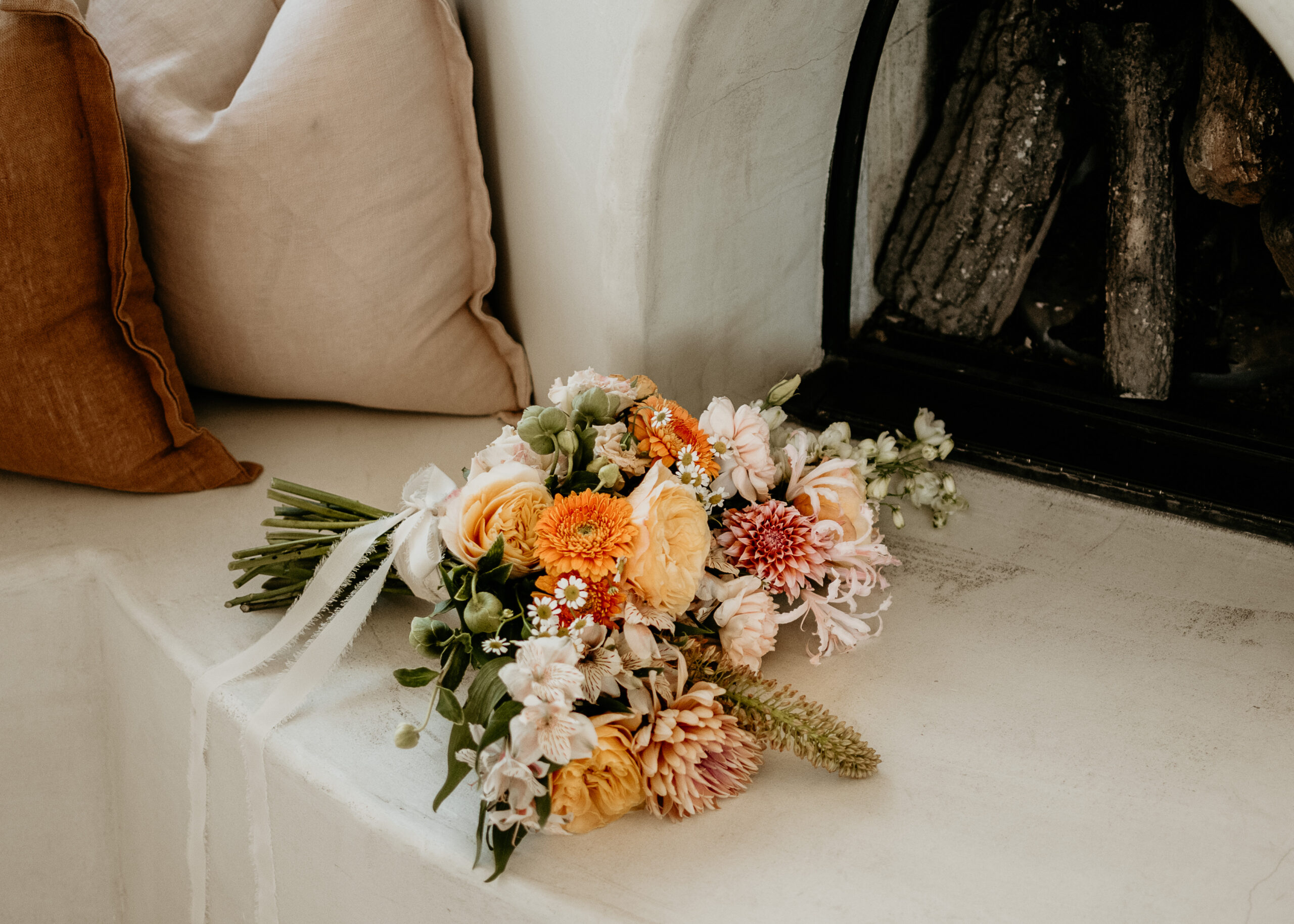 Bridal bouquet in peach, orange, and white resting on a cushioned bench, a finished piece from wedding florist services