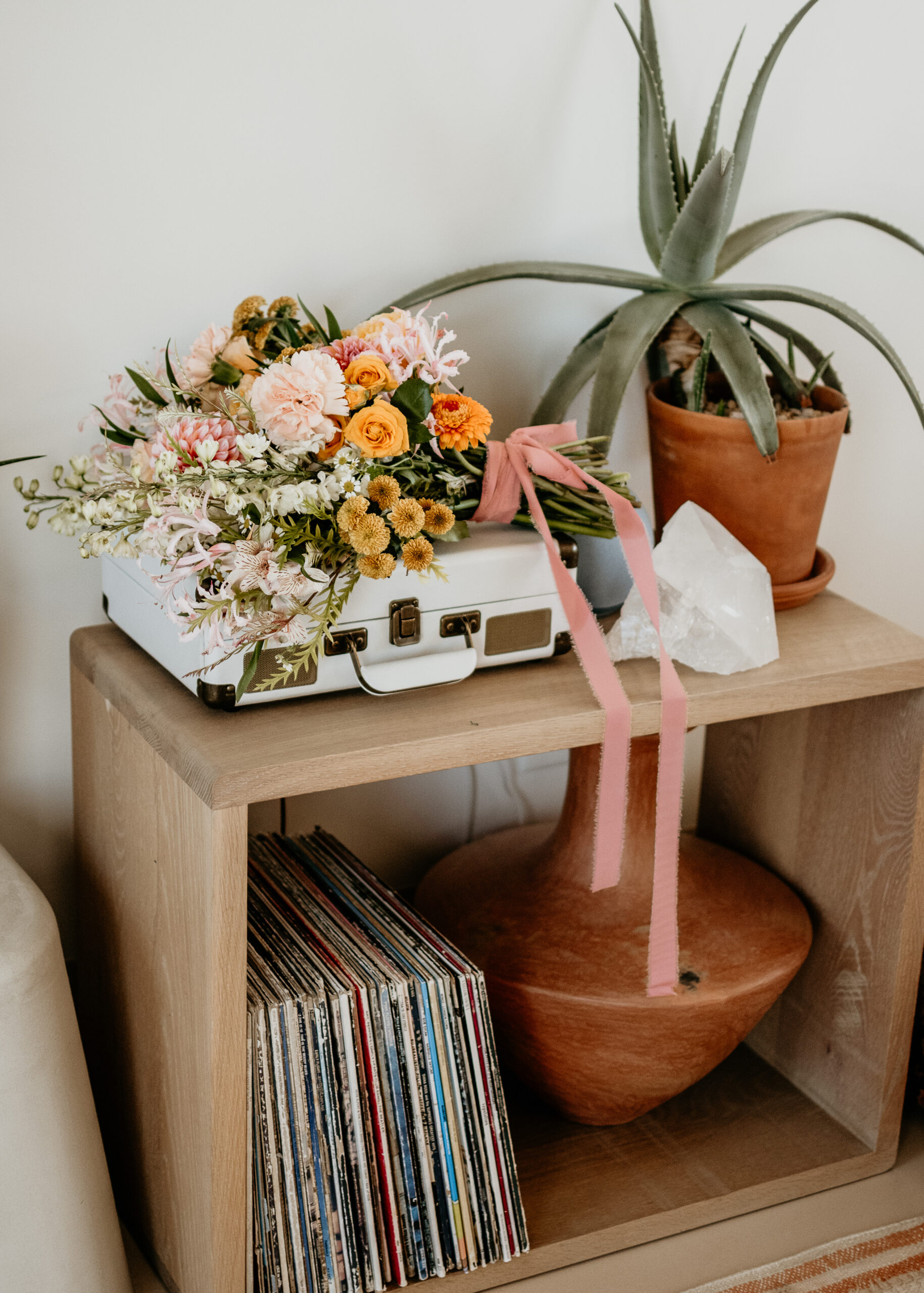 Bouquet with pink ribbon on a vintage record player atop a wood shelf, styled as part of wedding florist services