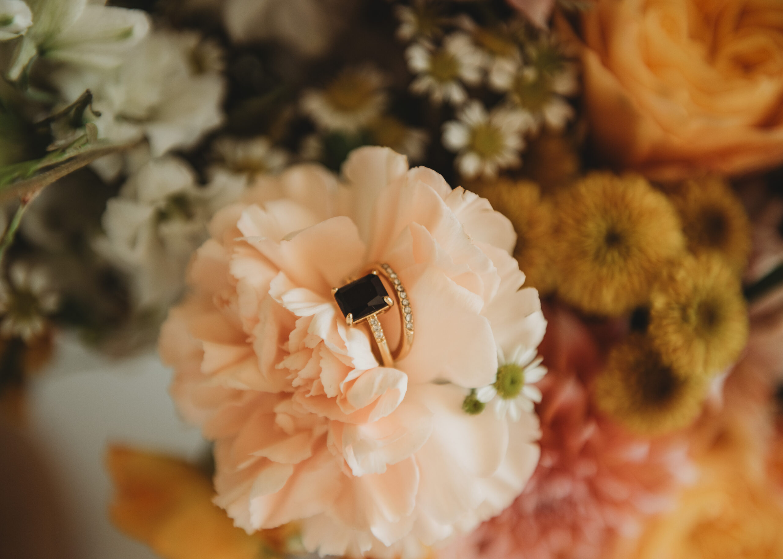 Wedding rings resting on a soft peach bloom in a close-up of a bridal bouquet, a detail of wedding florist services